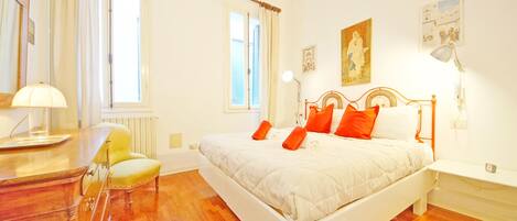 A bedroom with a bed, bedside table, lamp, chair, and a window with curtains.