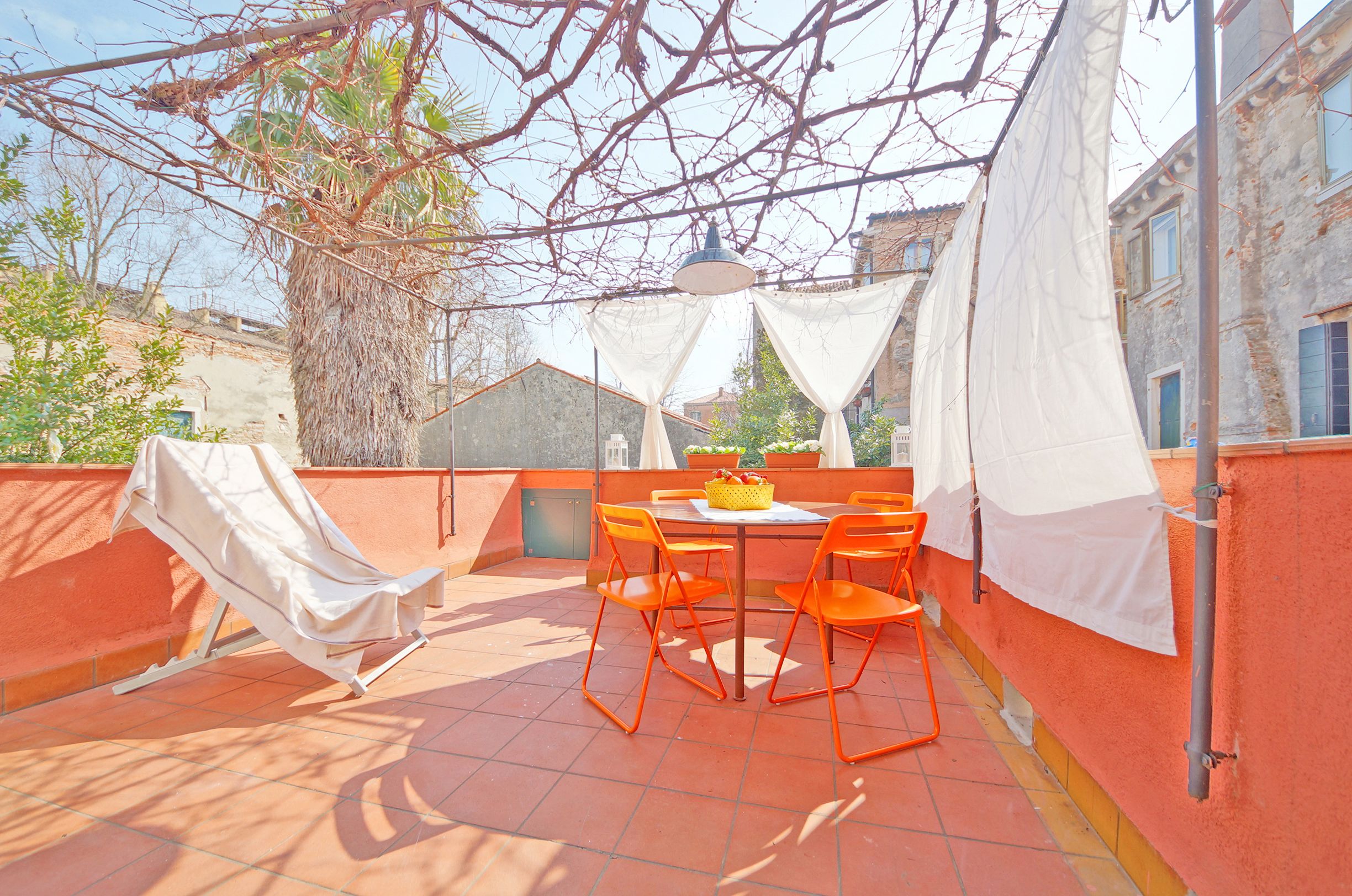 An outdoor patio with a table and chairs, a covered seating area, and a view of buildings in the background.