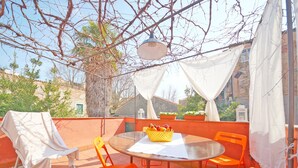 An outdoor patio with a round table, orange chairs, a covered seating area, and a basket of fruit. - DolceVita Apartments N. 241 (Venice)