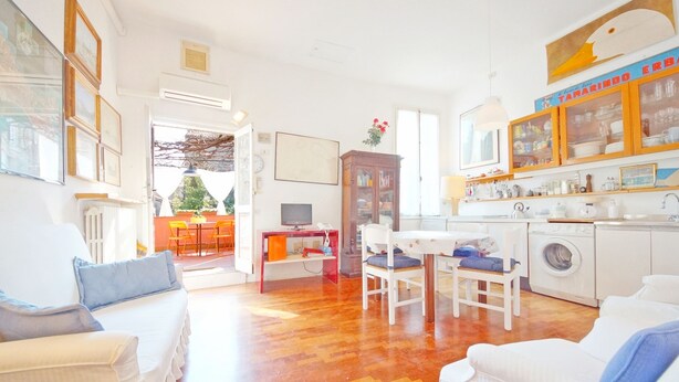 A bright living room with a sofa, a dining table, and a kitchen area with a washing machine. - DolceVita Apartments N. 241 (Venice)