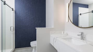 A modern bathroom with a glass shower enclosure, a white sink with a marble countertop, and a dark blue textured wall.