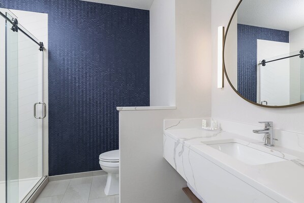 Un baño moderno con cabina de ducha de vidrio, un lavamanos blanco sobre encimera de mármol y una pared azul oscuro con textura.