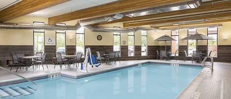 A swimming pool with a lifeguard chair, pool lift, and lounge area with chairs and umbrellas.