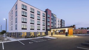 Un hôtel à plusieurs étages doté d’une façade moderne, d’une entrée bien éclairée et d’un parking accessible aux personnes handicapées.