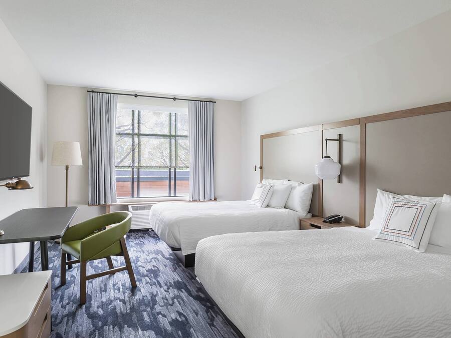 A hotel room with two beds, a desk, a chair, a TV, and a window with curtains.
