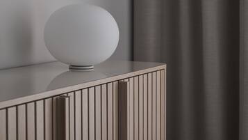 Una habitación moderna y minimalista con una lámpara cilíndrica elegante sobre una consola blanca.