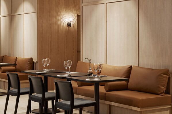 A modern dining area with a sofa and chairs, a table with glasses and a vase, and a wall-mounted light fixture.