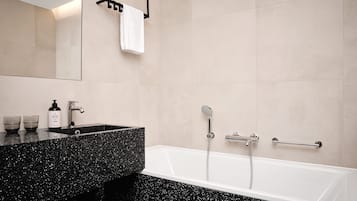 Un baño moderno con encimera de aspecto moteado negro, una bañera blanca y un espejo grande.