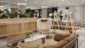 A modern lounge area with wicker furniture, a wooden bench, and a small table with a plant. - Original Sokos Hotel Tripla (Helsinki)