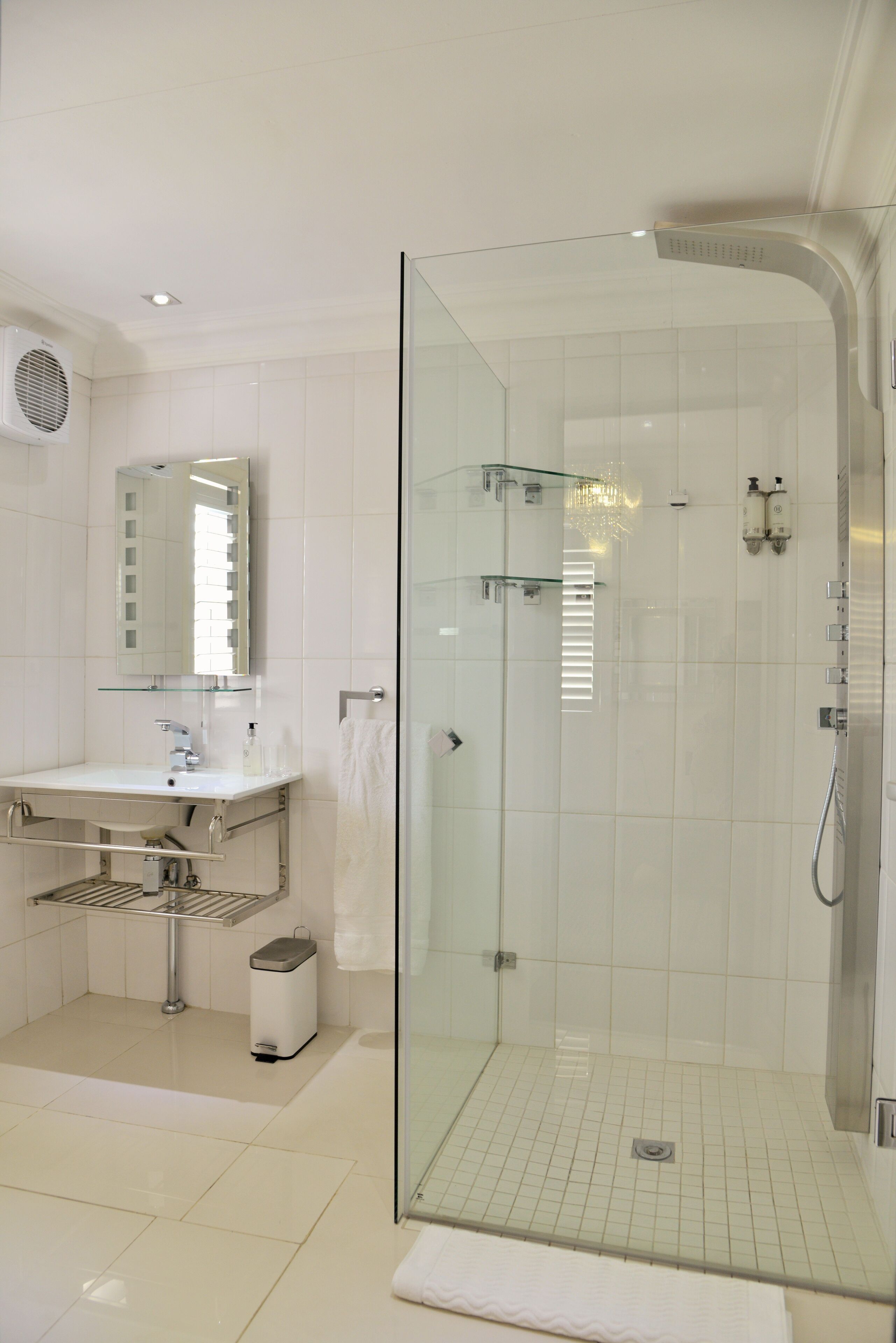 A modern bathroom with a glass-enclosed shower, a white sink with a mirror, and a towel rack.