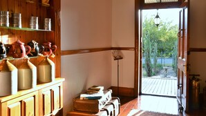 A room with wooden cabinets displaying ceramic items, a door leading to an outdoor area with a view of greenery, and a small table with books. - Die Kliphuis Standerton (Lekwa)