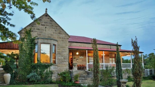 A stone house with a red roof, a porch, and a garden with a birdbath. - Die Kliphuis Standerton (Lekwa)