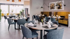 Un espace de restauration moderne avec des tables rondes, des chaises à revêtement gris et des luminaires suspendus.