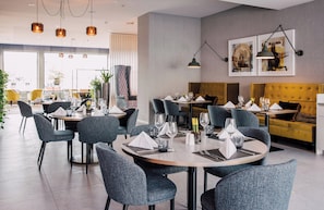 Un espace de restauration moderne avec des tables rondes, des chaises à revêtement gris et des luminaires suspendus.