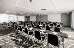 Ein Konferenzraum mit Tischen, Stühlen, einer Projektionsleinwand und einem großen Fenster.