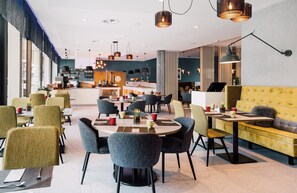 A modern hotel lobby with round tables, comfortable seating, and a central bar area. - Leonardo Hotel Zurich Airport (Kloten)