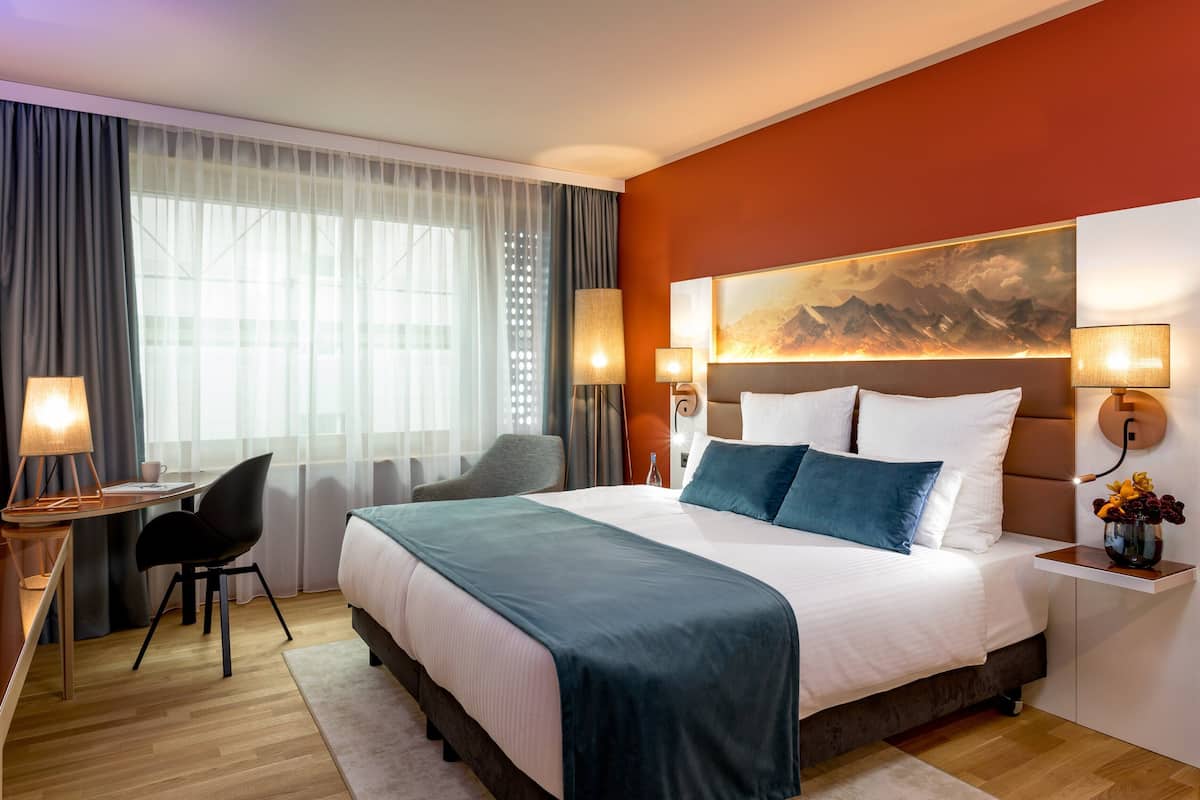 Une chambre d’hôtel avec un grand lit, un bureau avec une chaise, une table de chevet avec une lampe et un tableau au mur.