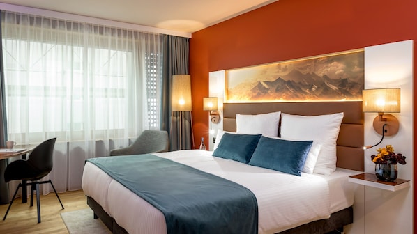 Une chambre d’hôtel avec un lit, un bureau, une chaise et un grand tableau au mur.