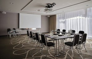 A conference room with a projector screen, tables, chairs, and a carpeted floor.
