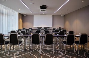 Une salle de conférence dotée d’un grand écran de projection, de rangées de chaises et d’un sol recouvert de moquette.
