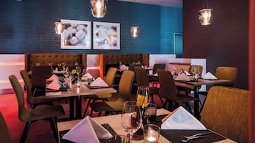 L’intérieur d’un restaurant, avec des tables dressées pour le service, des chaises et des lampes suspendues.