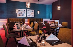 L’intérieur d’un restaurant, avec des tables dressées pour le service, des chaises et des lampes suspendues.