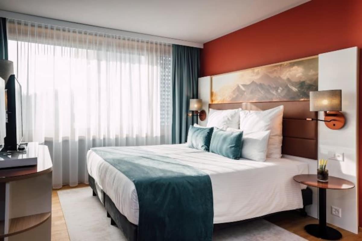 Een hotelkamer met een groot bed, een bureau, een stoel, een lamp en een schilderij aan de muur.