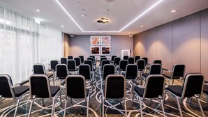 Une salle de conférence avec des rangées de chaises, un pupitre et une grande fenêtre avec des rideaux.