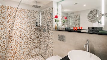 Ein modernes Badezimmer mit einer Duschwand aus Mosaik, einem großen Spiegel und einem Waschbecken mit schwarzer Arbeitsplatte.