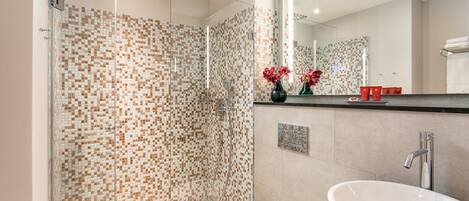 A modern bathroom with a glass shower enclosure, a white sink, and a mirror above the counter.