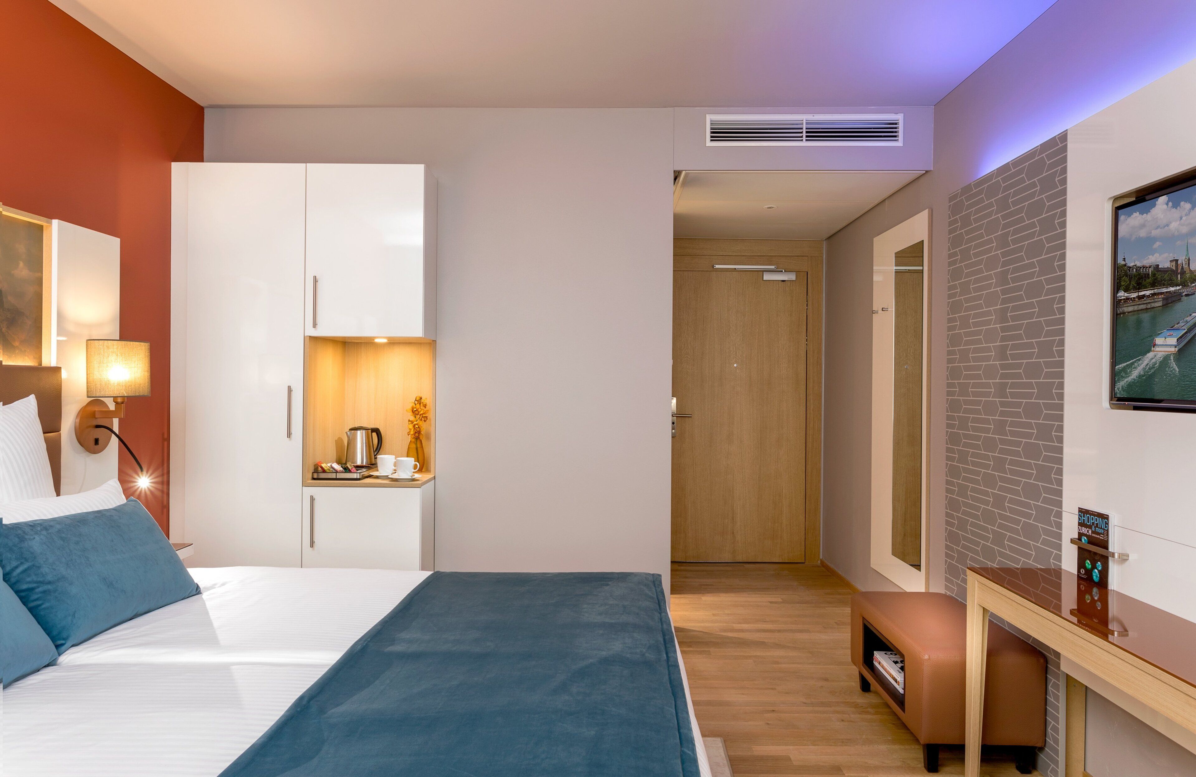 A modern hotel room with a bed, a desk, a coffee station, and a view of a river.