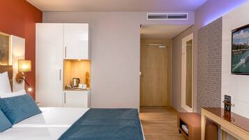 A modern hotel room with a bed, a desk, a coffee station, and a view of a river.