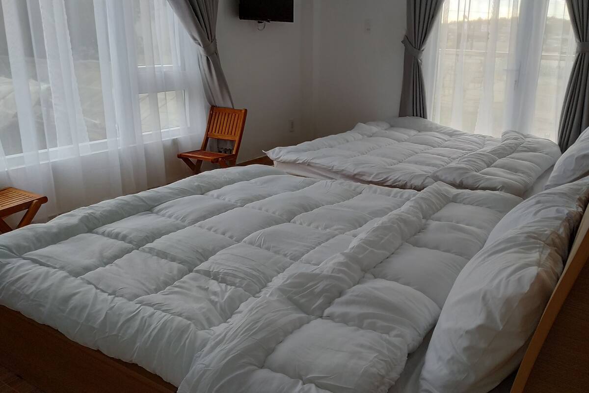 A hotel room with a large bed, a wooden chair, and a TV mounted on the wall.