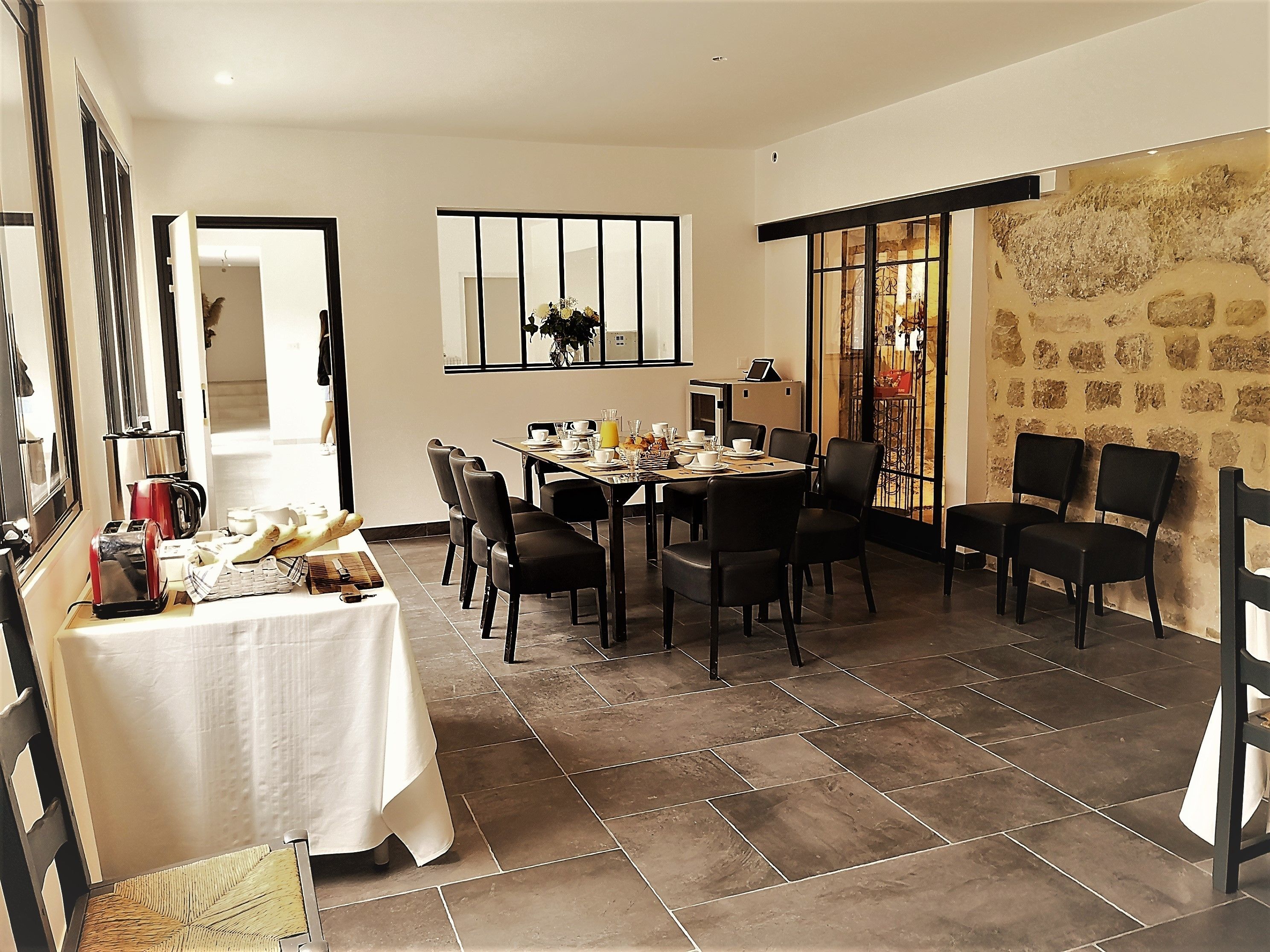 Un coin repas avec une table dressée pour six personnes, des chaises, une machine à café et une plante décorative.