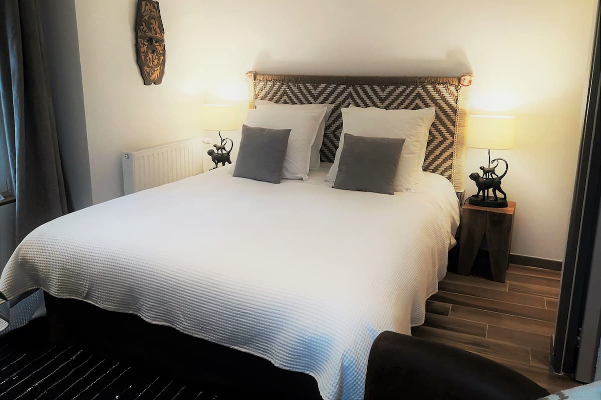A neatly made bed with a patterned headboard, two bedside lamps, and a radiator.