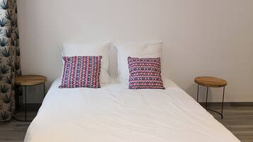 Una cama con ropa de cama blanca, dos almohadas estampadas y un cuadro de pared con un cactus.