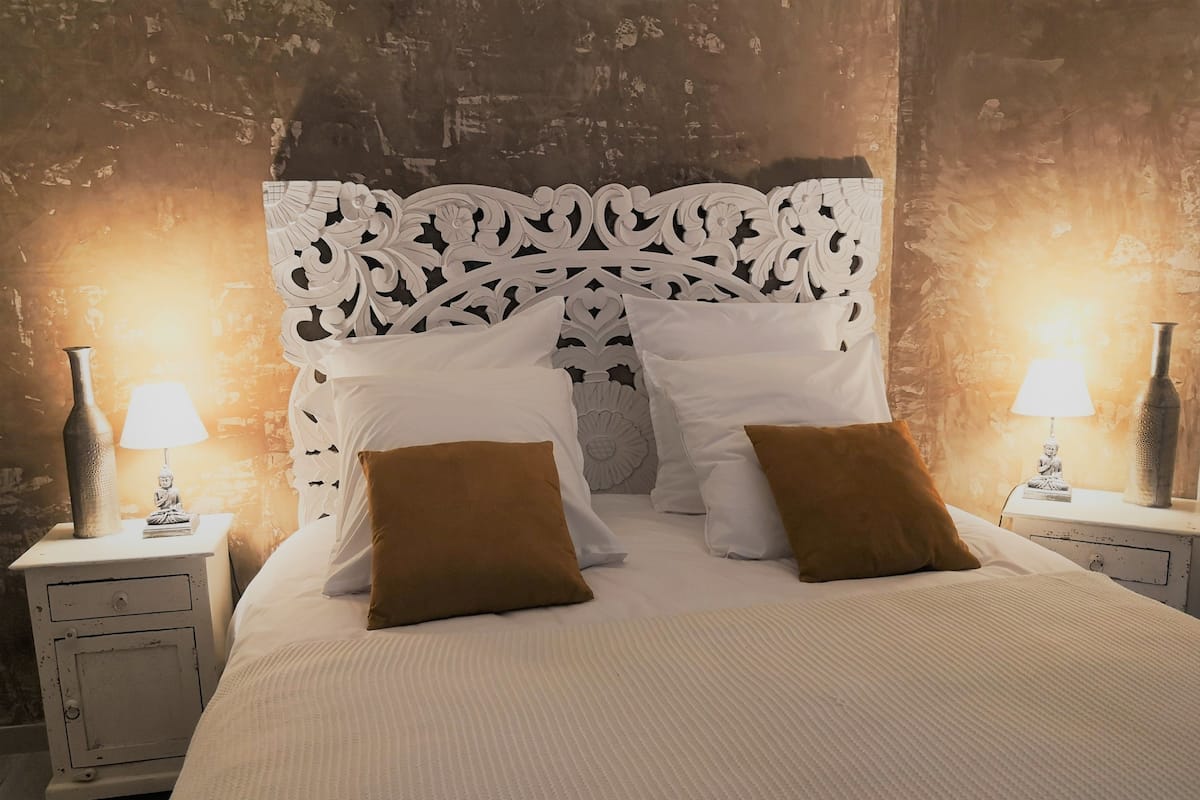 A bed with a white headboard, two brown pillows, and two bedside tables with lamps and decorative items.