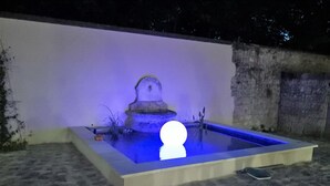 Une piscine rectangulaire avec une fontaine au centre, entourée d’un petit muret.