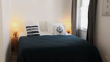 A neatly made bed with a dark blue bedspread and two pillows, one with a nautical design and another with a striped pattern. There are two bedside lamps with decorative vases on the nightstands.