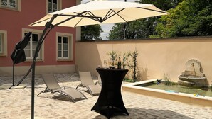 Une terrasse extérieure avec une table, des chaises, un grand parasol et une fontaine.