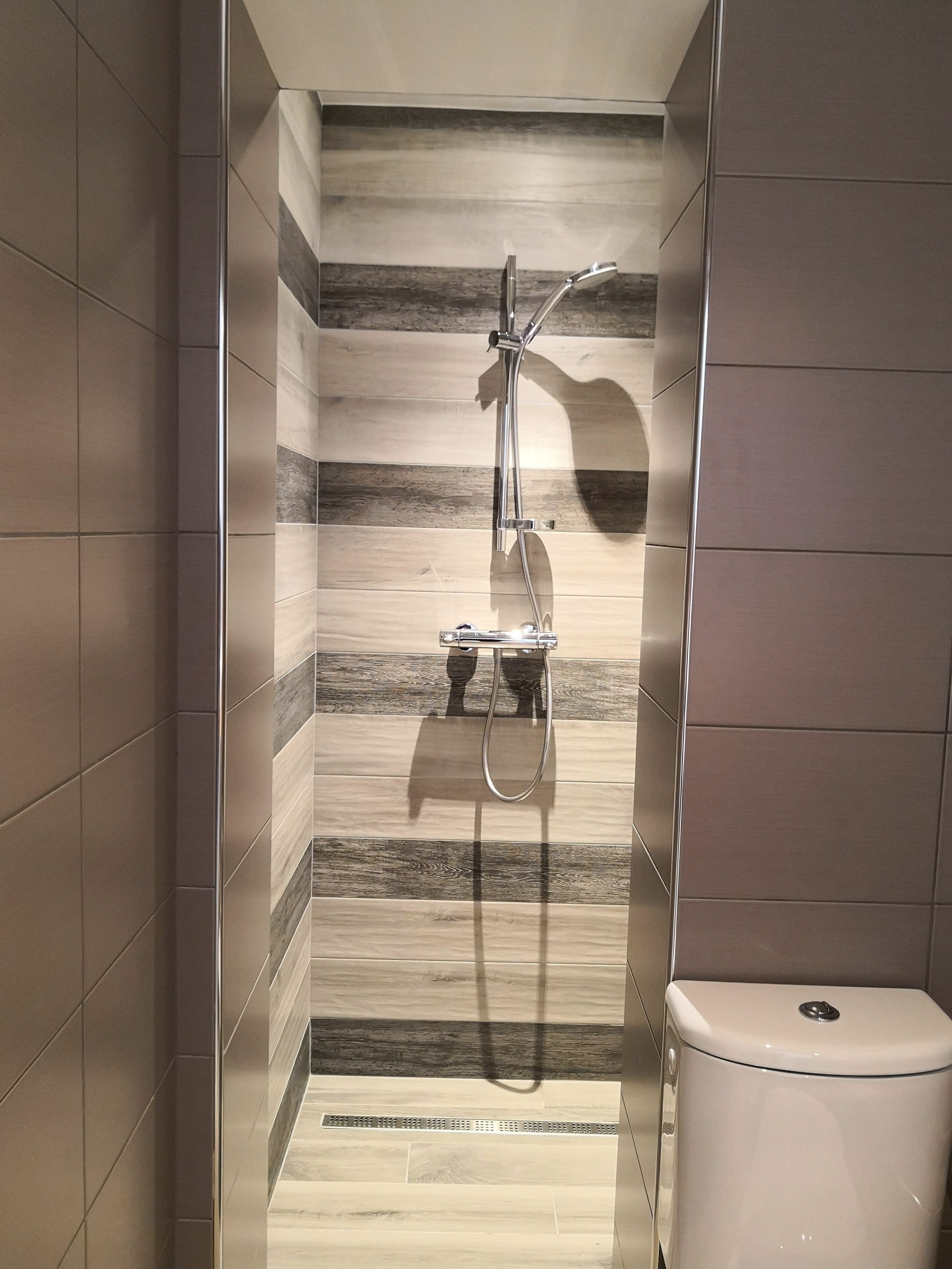 Une salle de bain avec une douche, des murs carrelés et des toilettes.