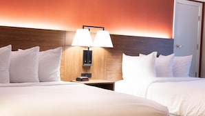 A hotel room with two beds, a nightstand with a lamp, and a wooden headboard.