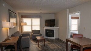 A furnished living room with a sofa, armchair, coffee table, and a TV on a fireplace mantel.