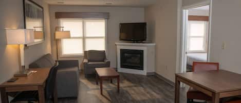 A furnished living room with a sofa, armchair, coffee table, and a TV on a fireplace mantel.