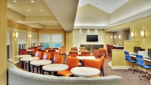 A hotel lobby with multiple seating areas, a flat-screen TV mounted on the wall, and a fireplace.