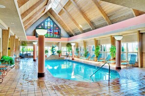 Una piscina interior con techo alto, vigas de madera y una ventana de vitral.