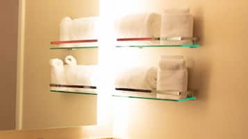 A bathroom with a granite countertop, a sink, and two glass shelves holding white towels.