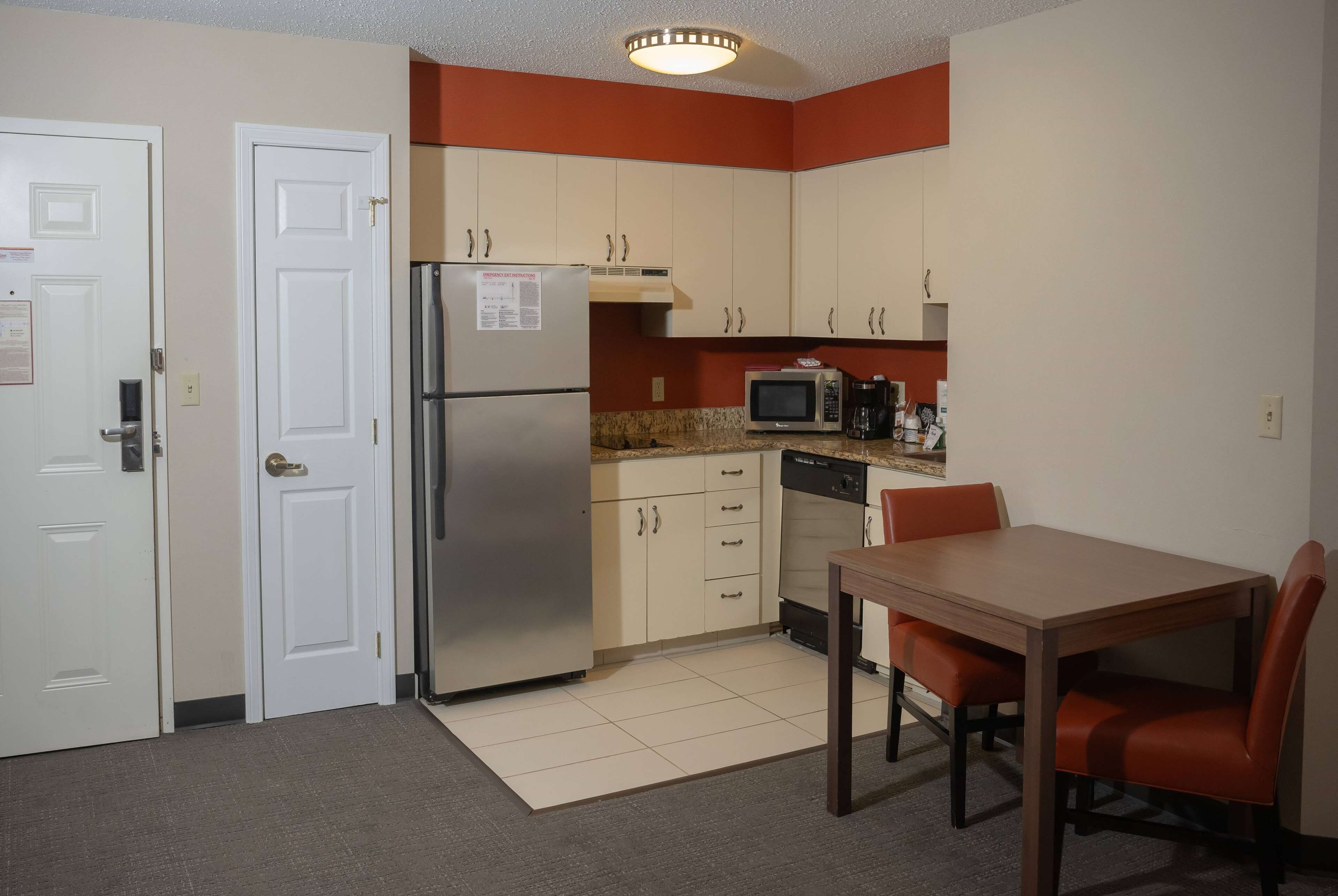 A compact kitchen with a refrigerator, microwave, and a dining table with chairs.