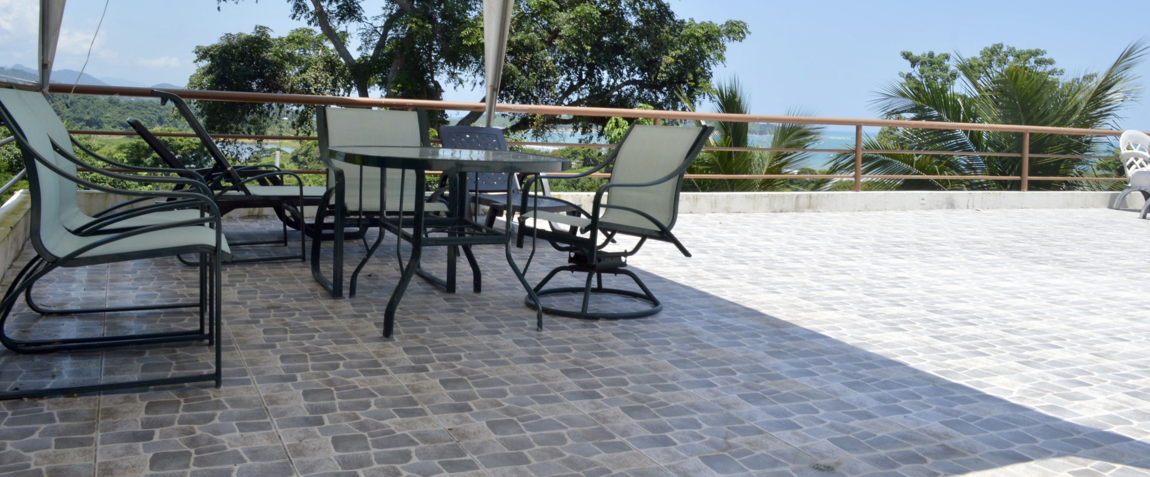An outdoor patio with a table and chairs, a railing, and a view of the ocean and trees.