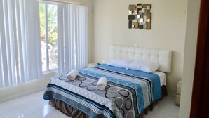 Een slaapkamer met een groot raam, een bed met een beddeken met een patroon, en een kunstwerk aan de muur.